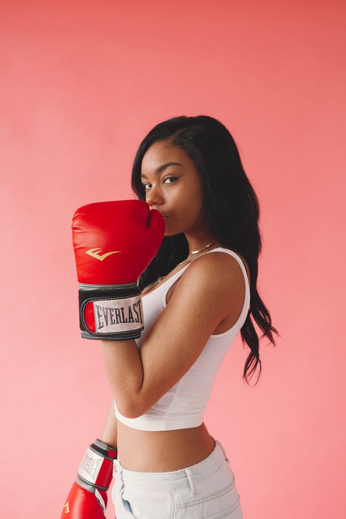 services-04 Stylish woman posing with red boxing gloves on a pink background, exuding confidence and fitness.