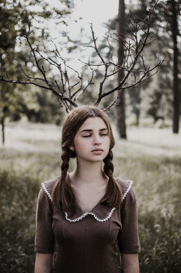 Artistic portrait of a girl with braided hair appearing to wear branches as antlers, creating an enchanting forest scene.
